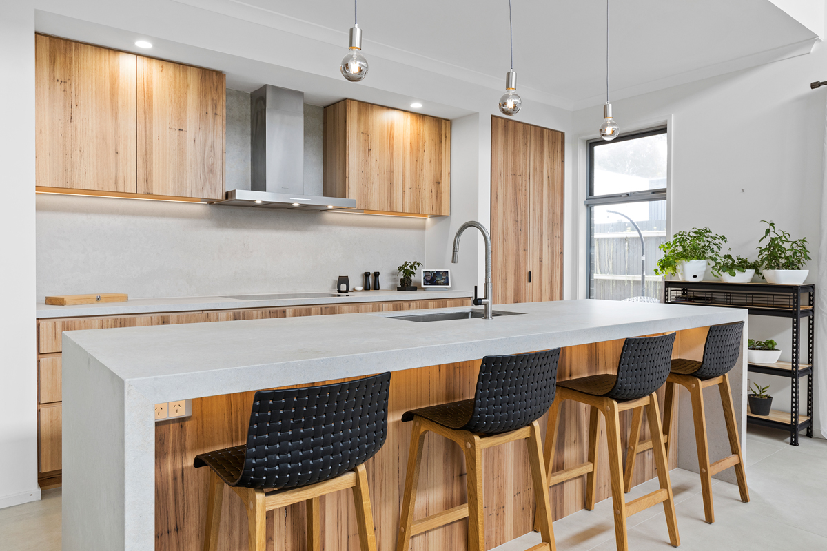 Island kitchen bench with grey stone top and black bar stool chairs